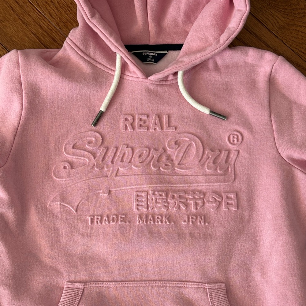 pink Superdry hoodie with an embossed (raised) logo design.